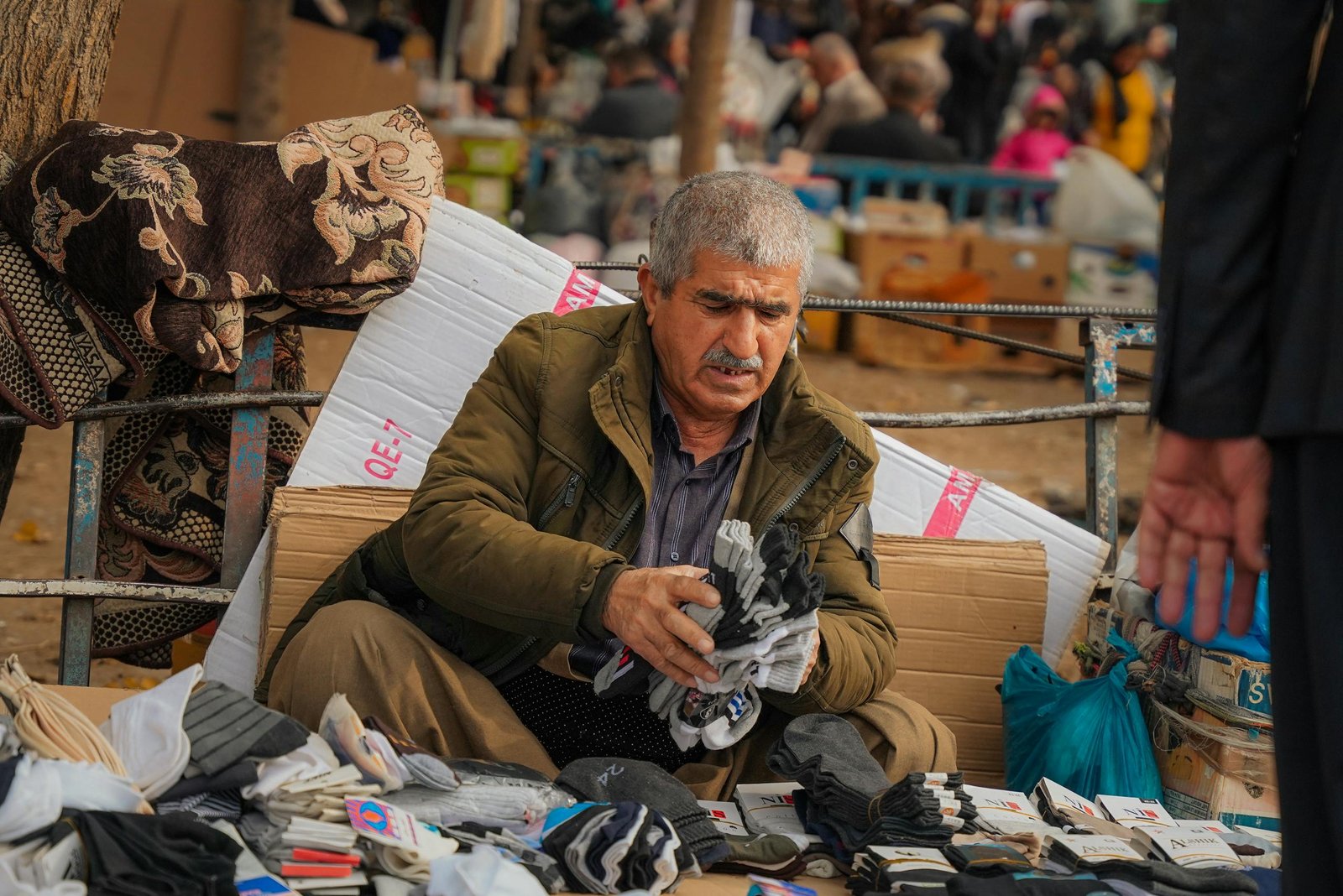 An elderly man sells socks at a bustling market in Sulaymaniyah, Iraq, showcasing local street life.