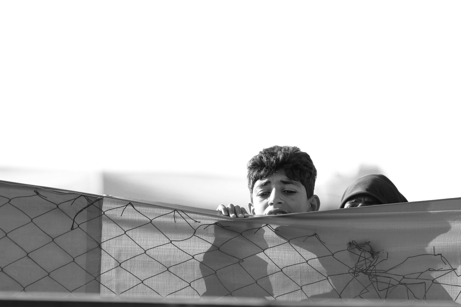Black and white image of a boy holding a fence, capturing emotion in Mosul, Iraq.